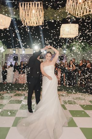 A couple shares their first dance under falling confetti and hanging lanterns.