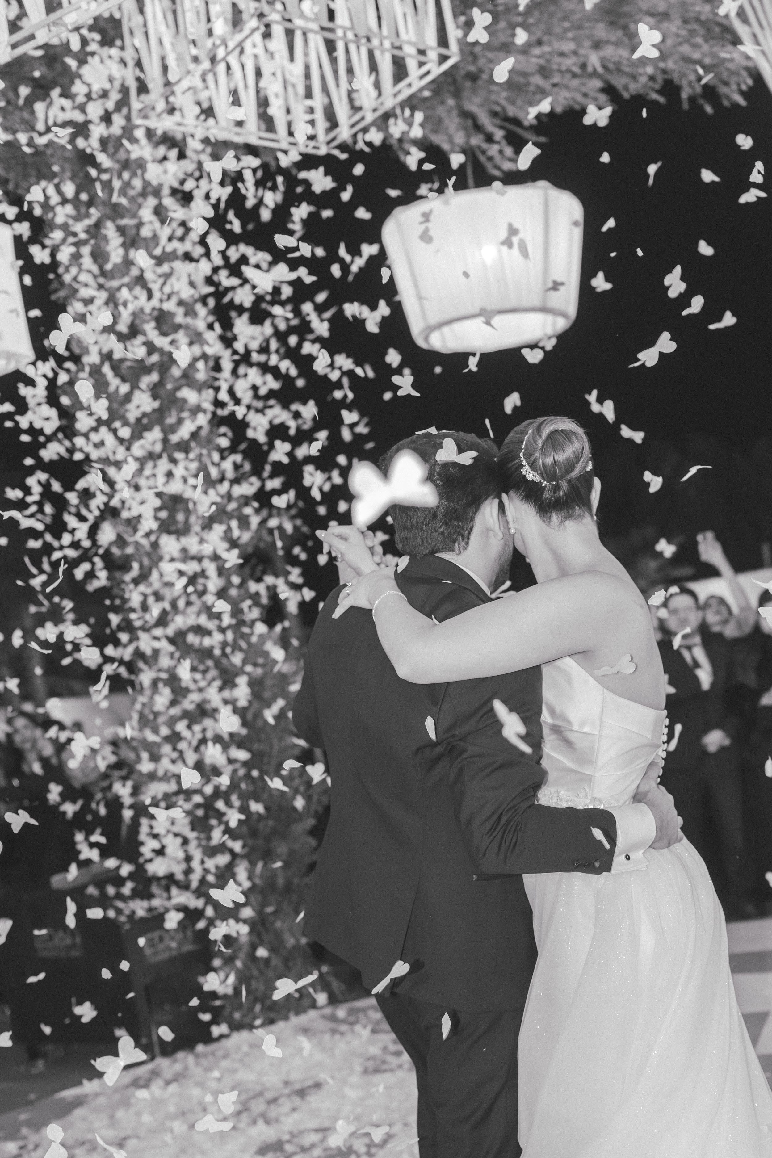 A black and white photo of newlyweds dancing amid falling confetti at their reception.