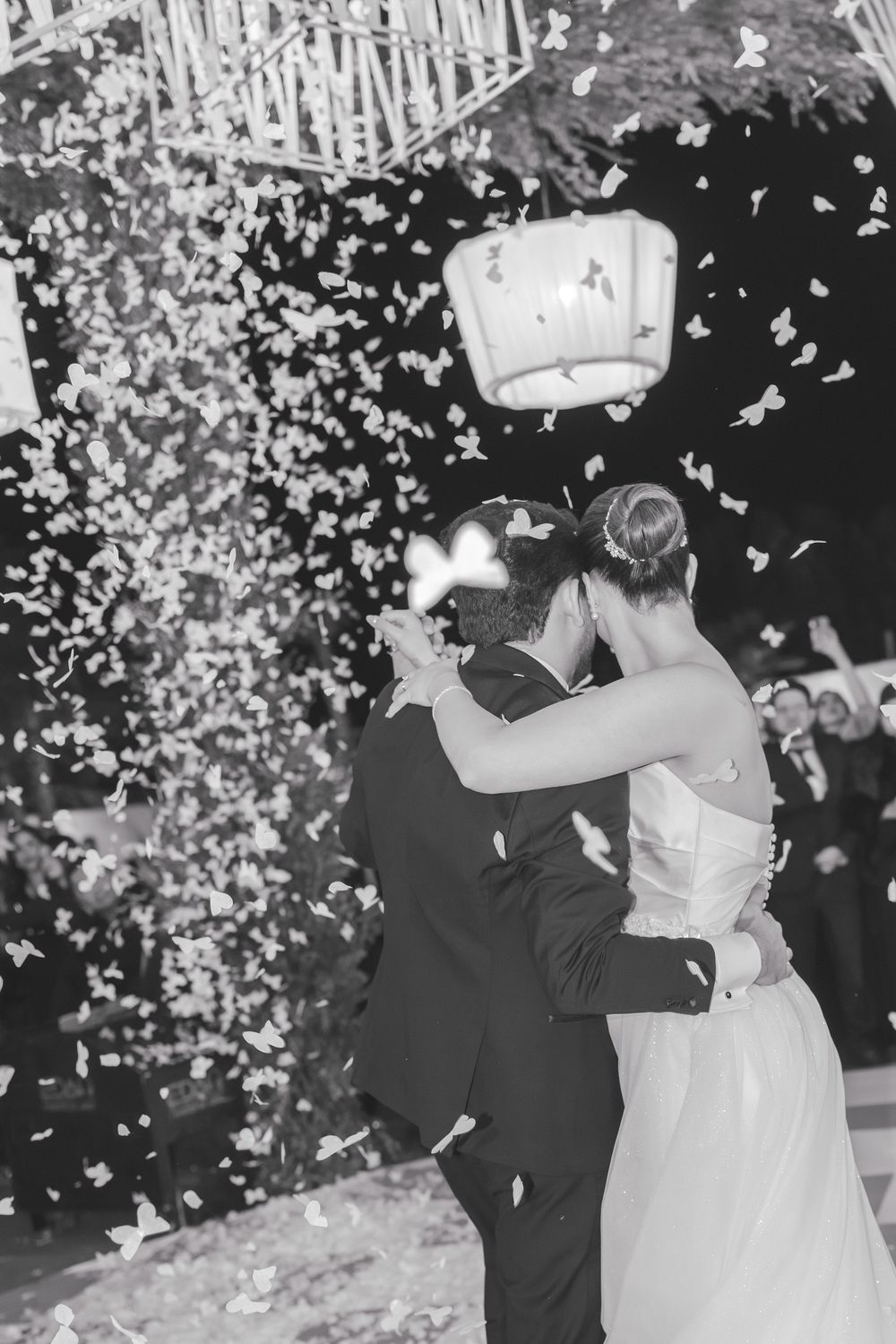 A black and white photo of newlyweds dancing amid falling confetti at their reception.
