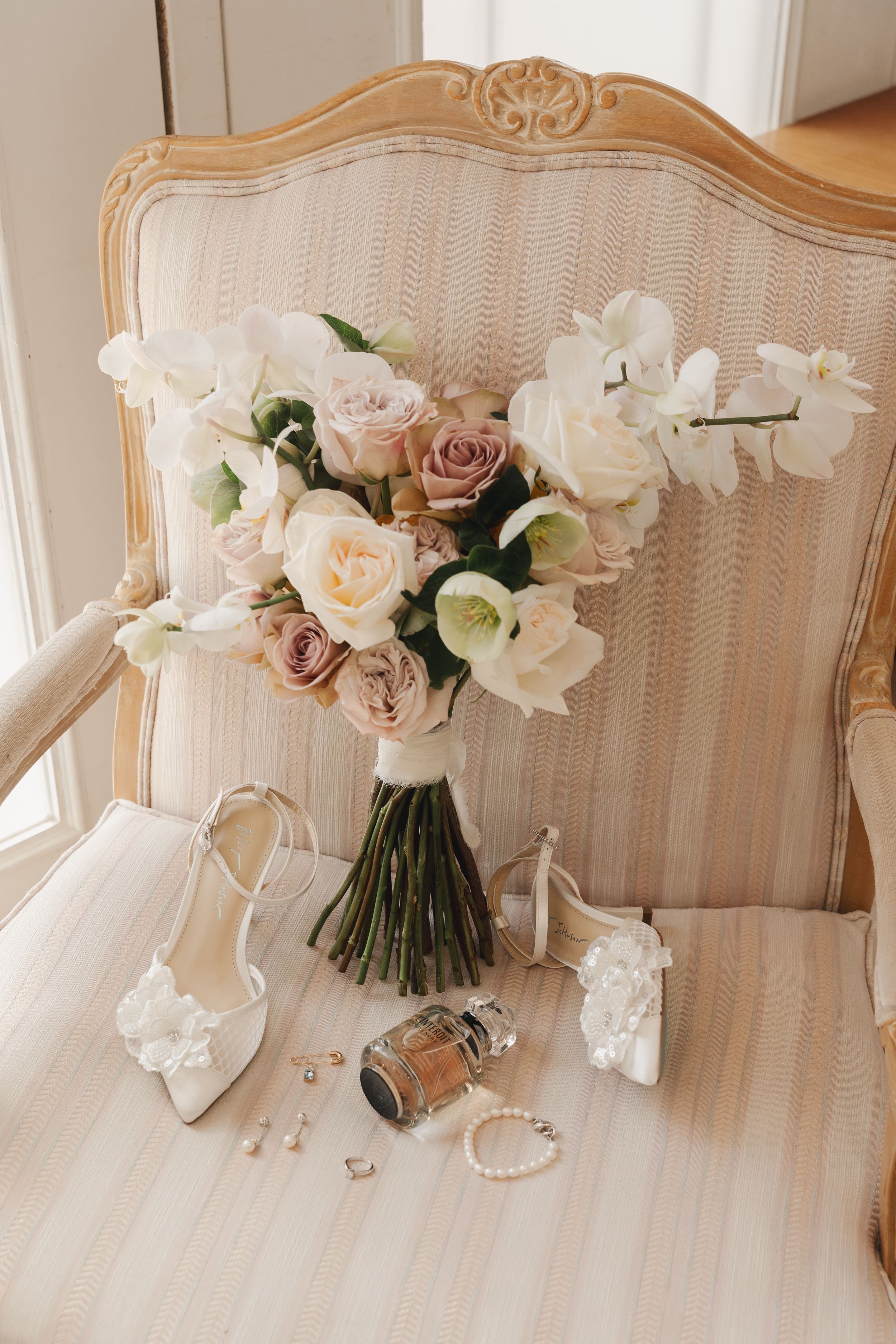Wedding accessories and floral arrangement displayed on vintage beige settee.
