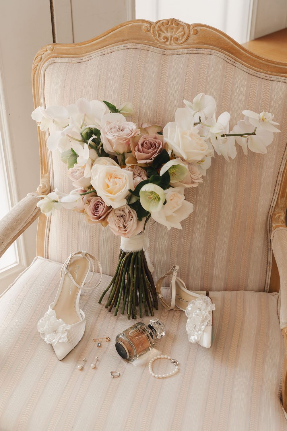 Wedding accessories and floral arrangement displayed on vintage beige settee.