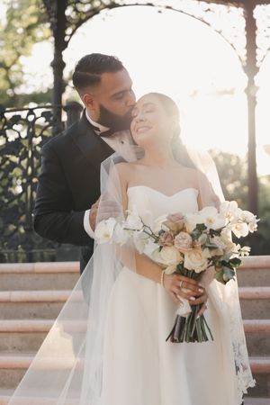 A romantic wedding portrait capturing a tender moment with a white floral bouquet.