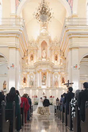 An ornate Catholic church interior during a wedding ceremony with guests in pews.