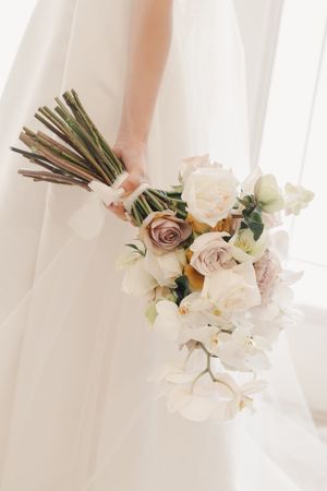 Ethereal wedding bouquet with white orchids and dusty rose flowers in natural light.