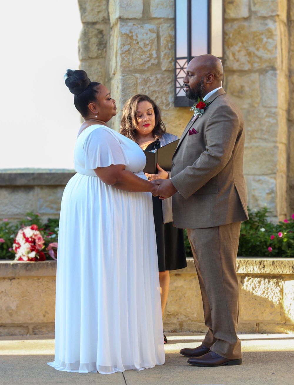A couple exchanges wedding vows with an officiant at a stone-walled outdoor venue.