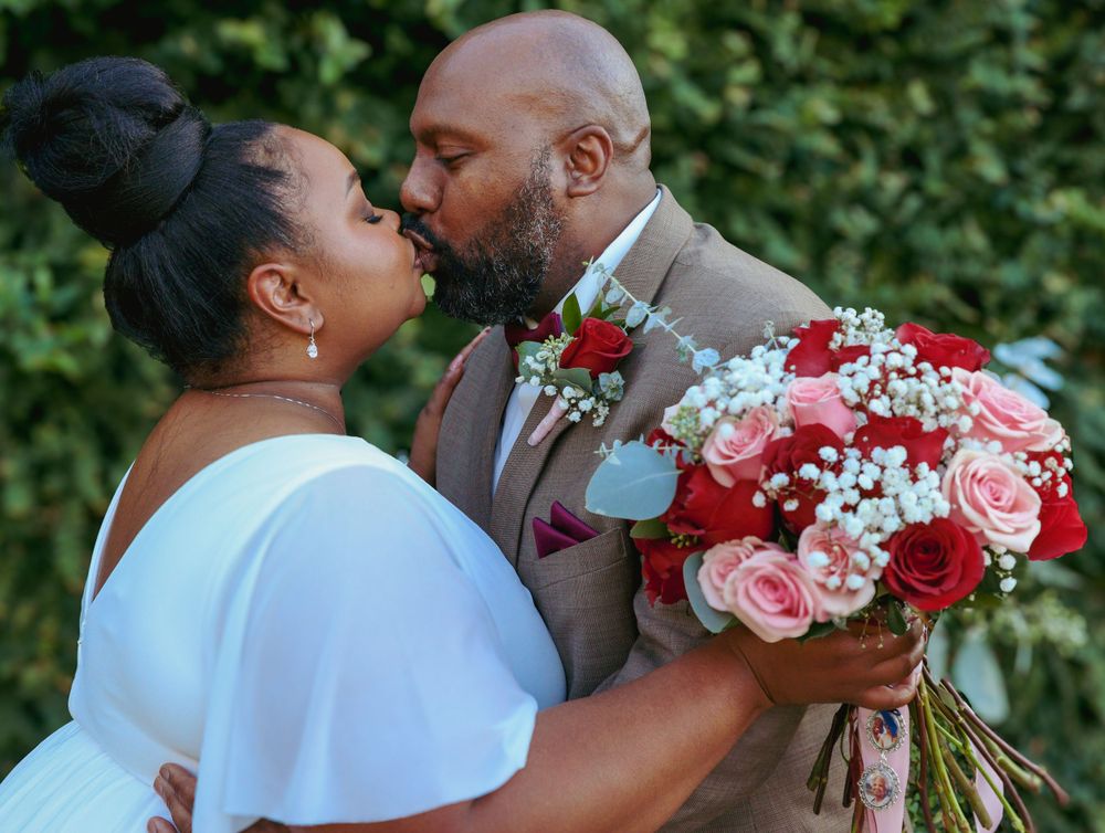 Couple shares romantic kiss while holding beautiful red and pink rose bouquet.