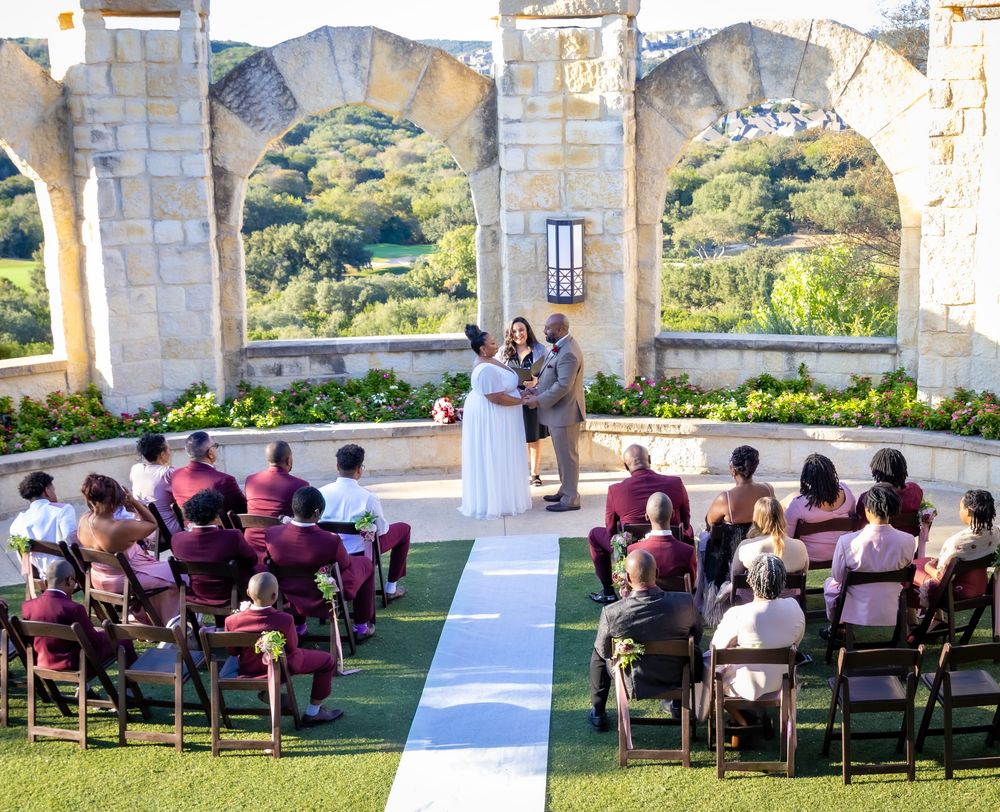 Wedding guests seated in burgundy chairs on a stone terrace overlooking a scenic mountain landscape.