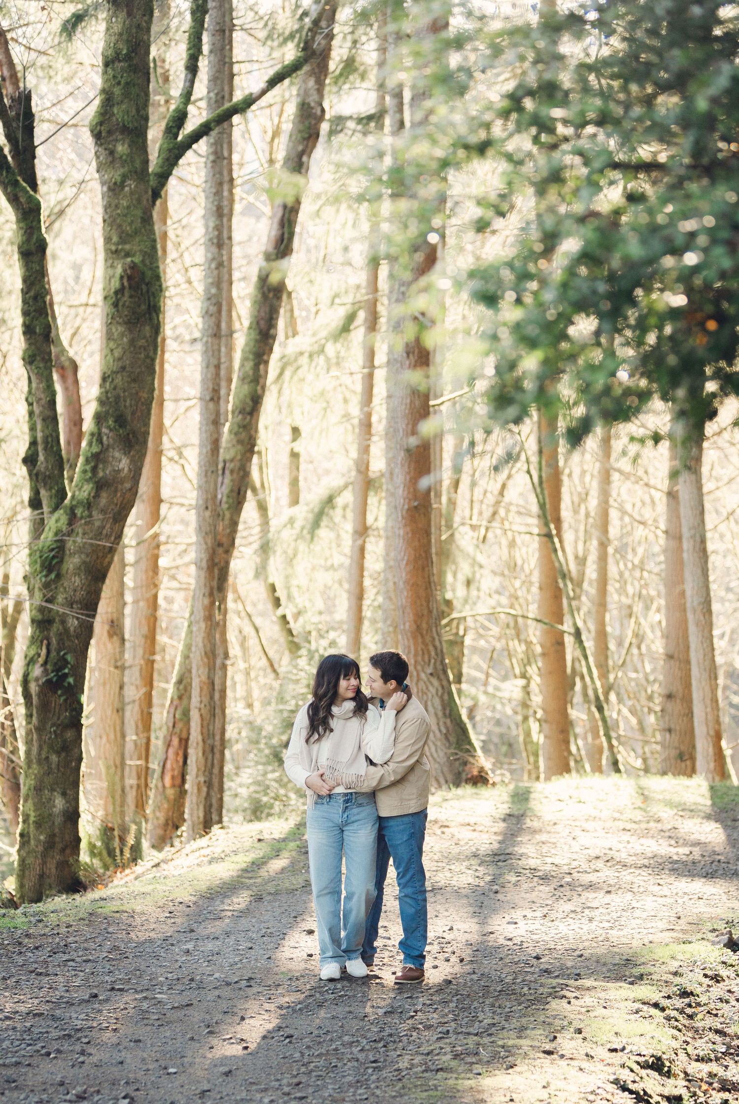 A couple walks hand in hand along a sunlit forest path surrounded by tall pine trees on a peaceful afternoon.