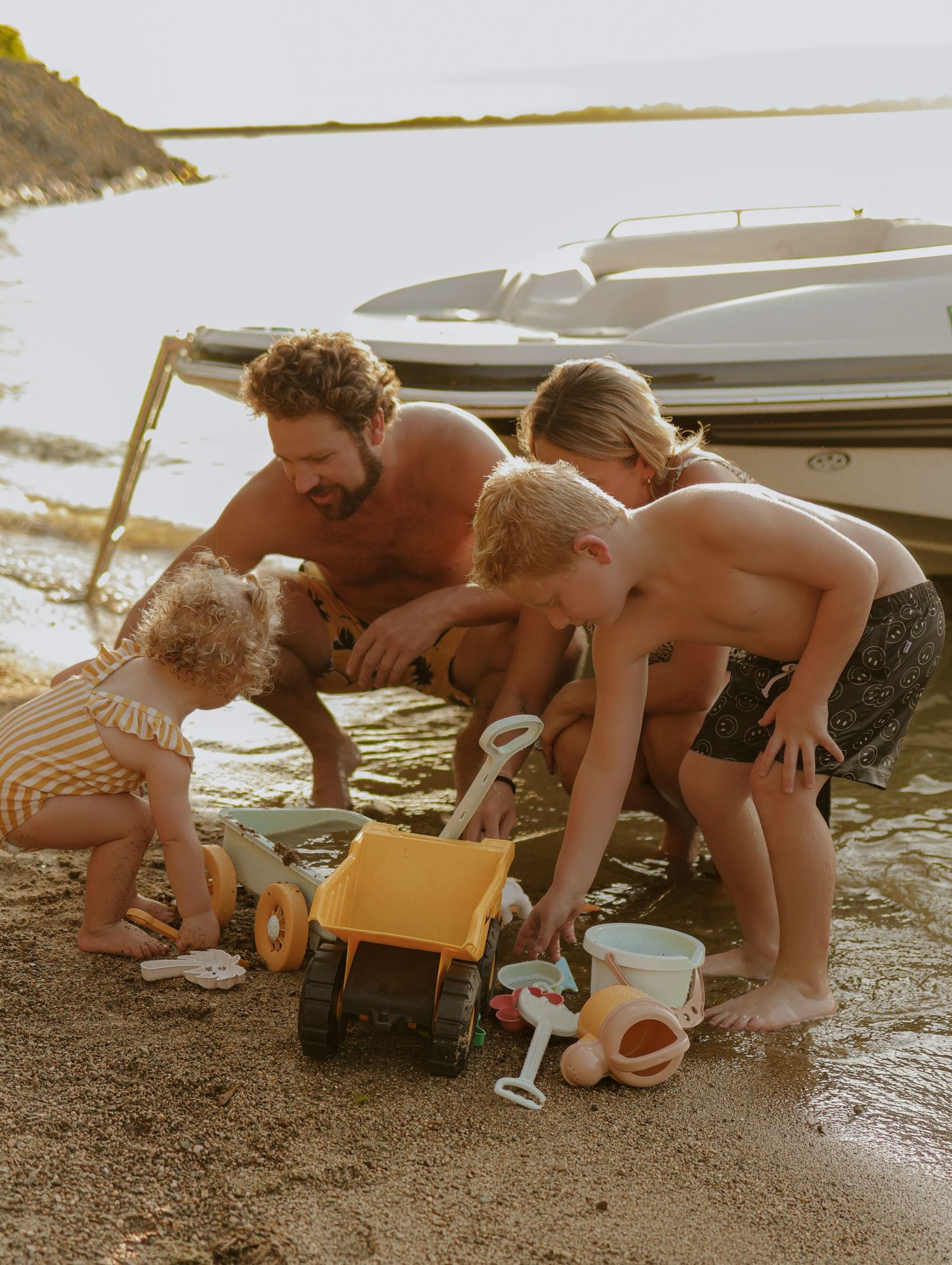 Children playing with toys on sandy beach near parked boat.
