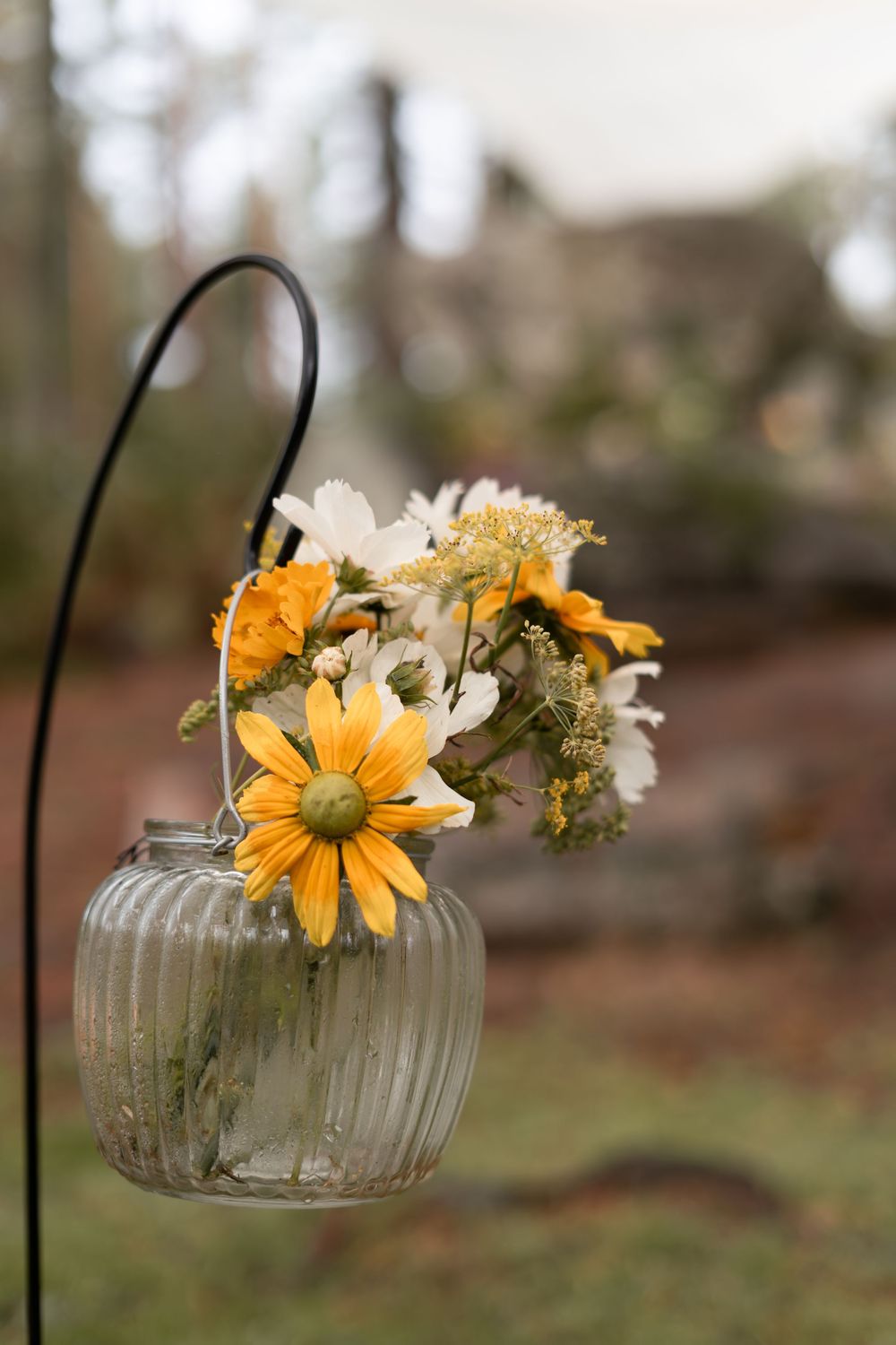 Delicate yellow daisies and white flowers arranged in a vintage glass jar against a blurred outdoor background.
