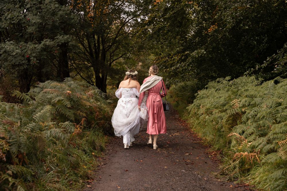 Wedding party walking down a wooded path surrounded by lush green foliage on an autumn day.
