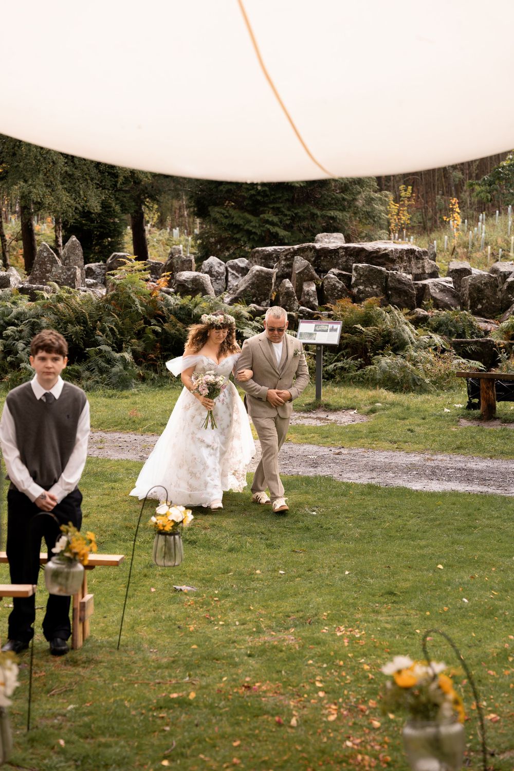 Wedding guests gather on a grassy lawn with scattered chairs and autumn decor at an outdoor celebration.
