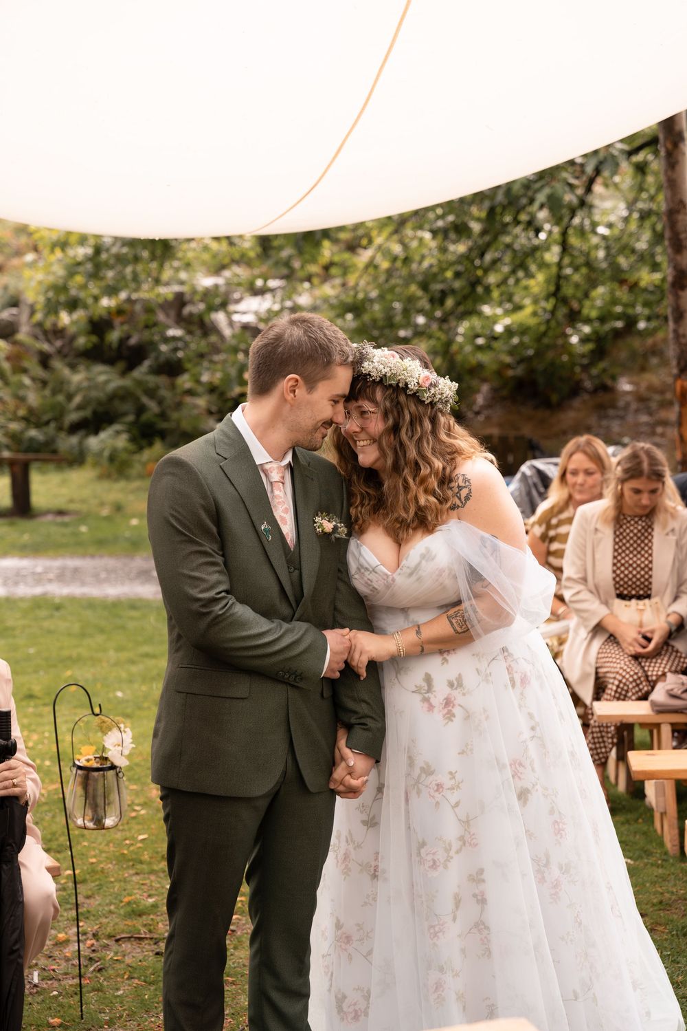 A romantic outdoor wedding scene with a couple dancing in a garden setting while guests look on from wooden benches.