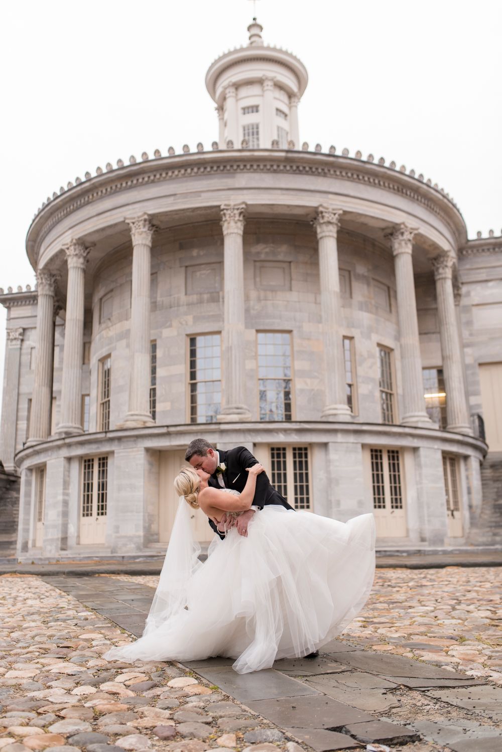 A romantic wedding couple shares a tender dip pose against the elegant backdrop of the Merchants Exchange Building in Philadelphia