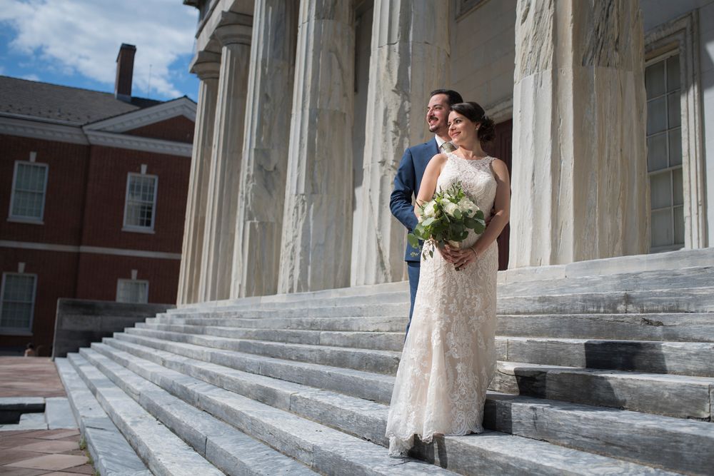 Wedding couple stands on grand marble steps of the 2nd Bank Building in Philadelphia with white columns on a sunny day.