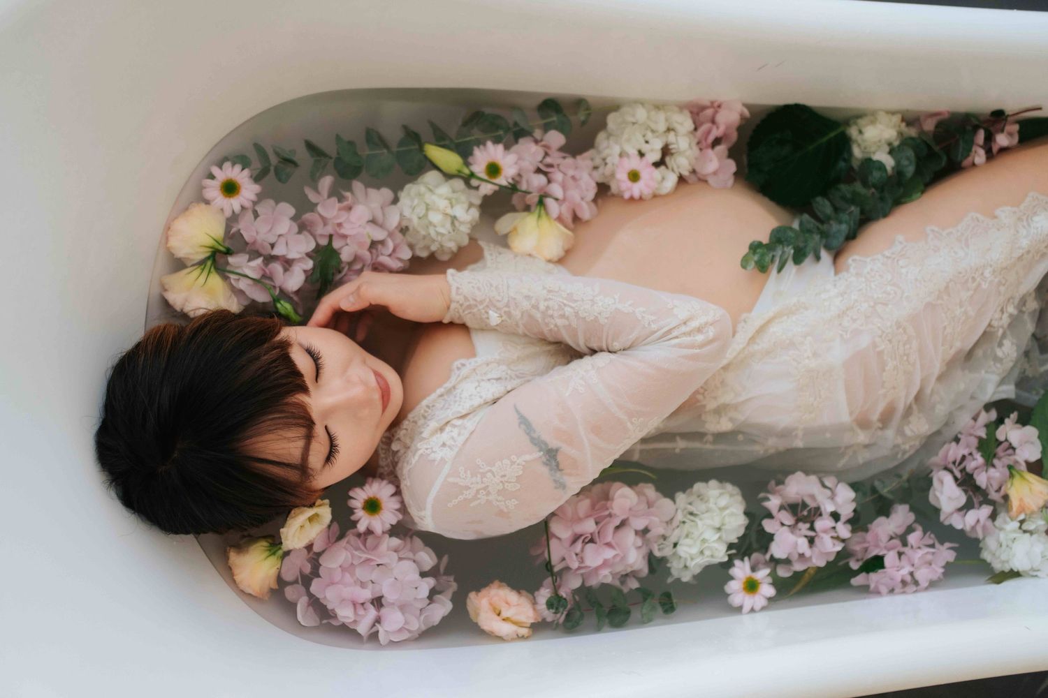 Person lying in vintage clawfoot bathtub filled with pink and white flowers wearing romantic lace dress一位穿著浪漫蕾絲洋裝的女子躺在裝滿粉紅色和白色花朵的復古爪足浴缸中。