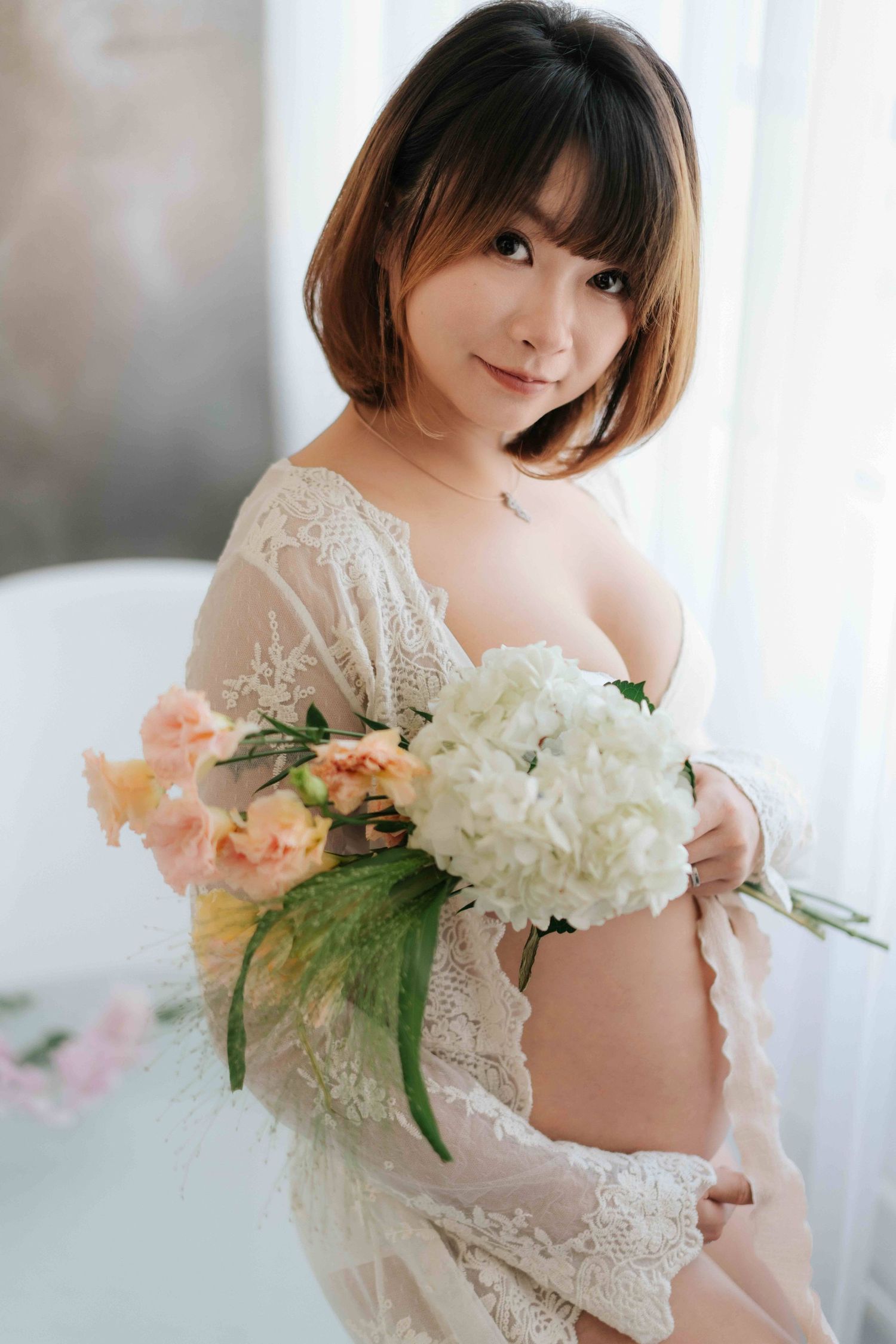 A person in black attire sits on a white bed near sheer curtains in a bright, minimalist setting.在明亮簡約的環境中，一位身穿黑色服裝的人坐在白色床上，床邊掛著薄紗窗簾。