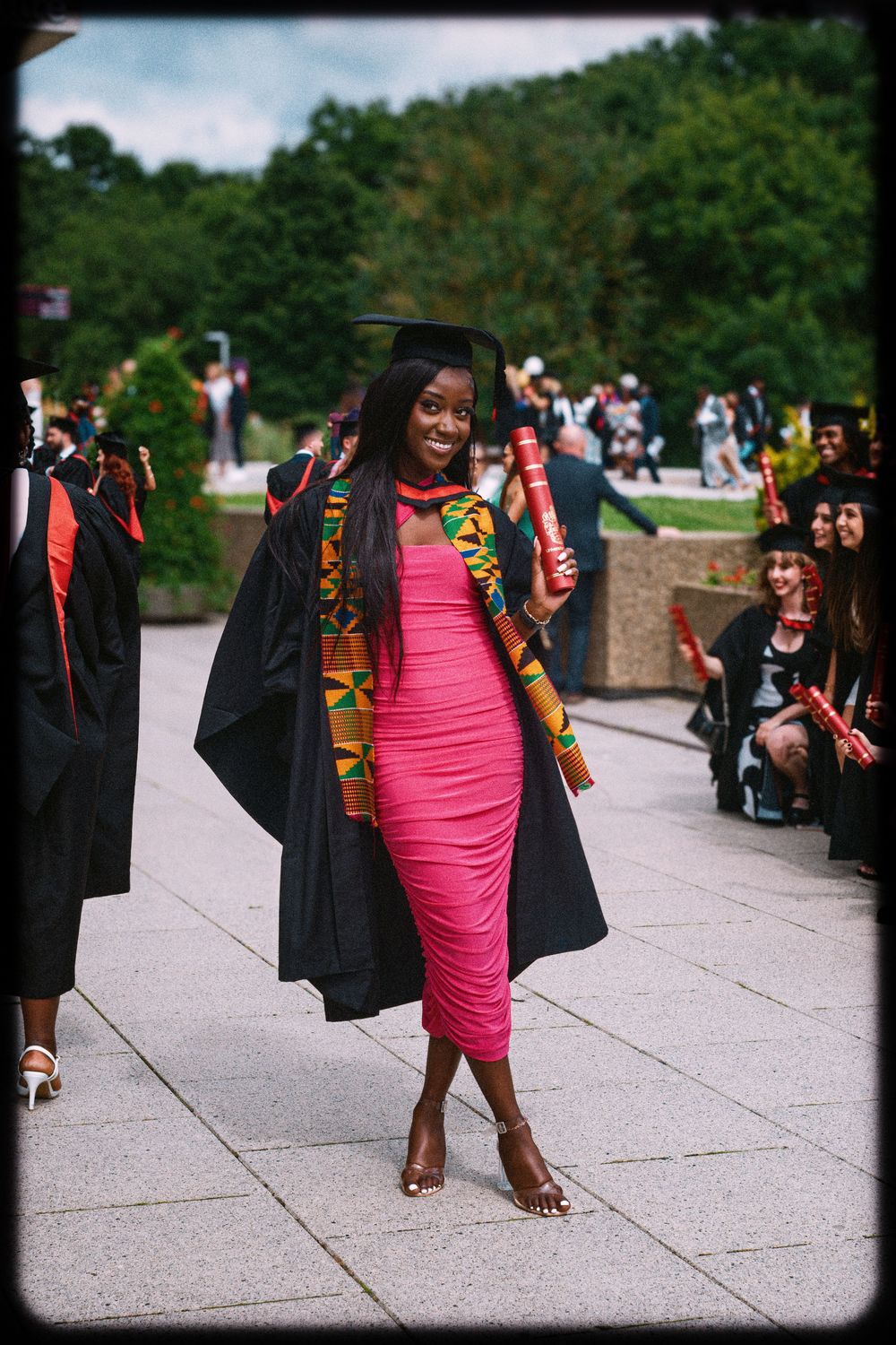 A sequence of graduation photos showing someone in a pink dress and academic regalia walking and posing outdoors.