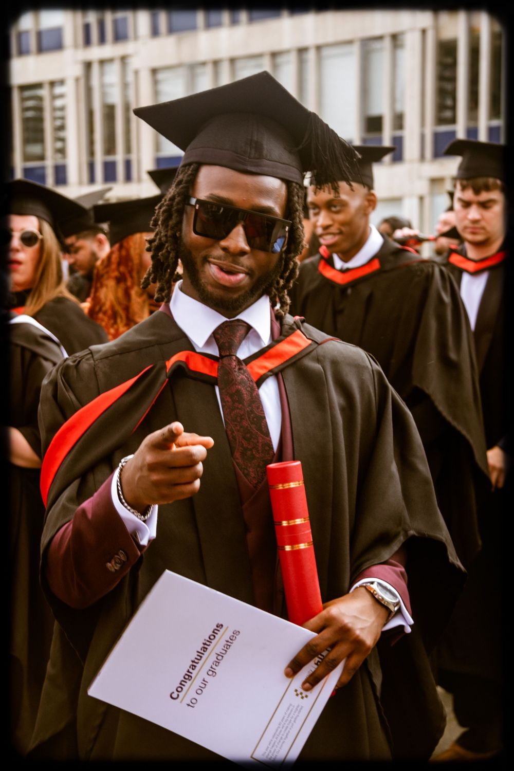 Graduate in black cap and gown holds up diploma during commencement ceremony.