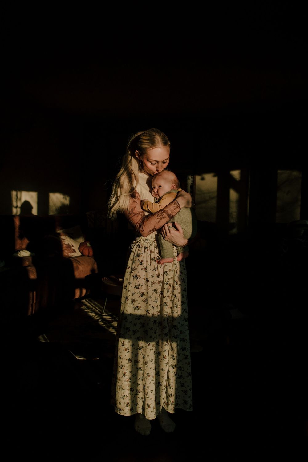 Silhouetted figures embracing in a dimly lit setting with floral dress visible.