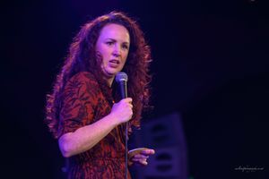 Performer with red hair singing passionately on stage in dramatic purple lighting during live performance.