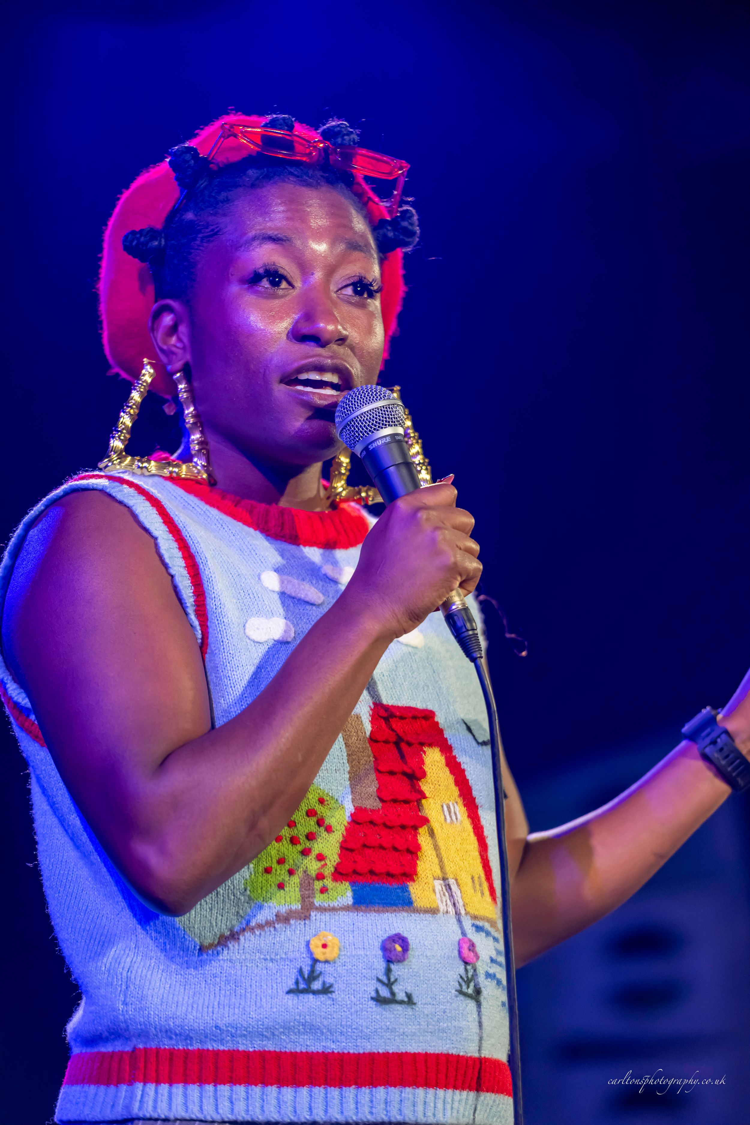 A performer in a white and red patterned vest sings passionately on stage under blue lighting during a concert performance.