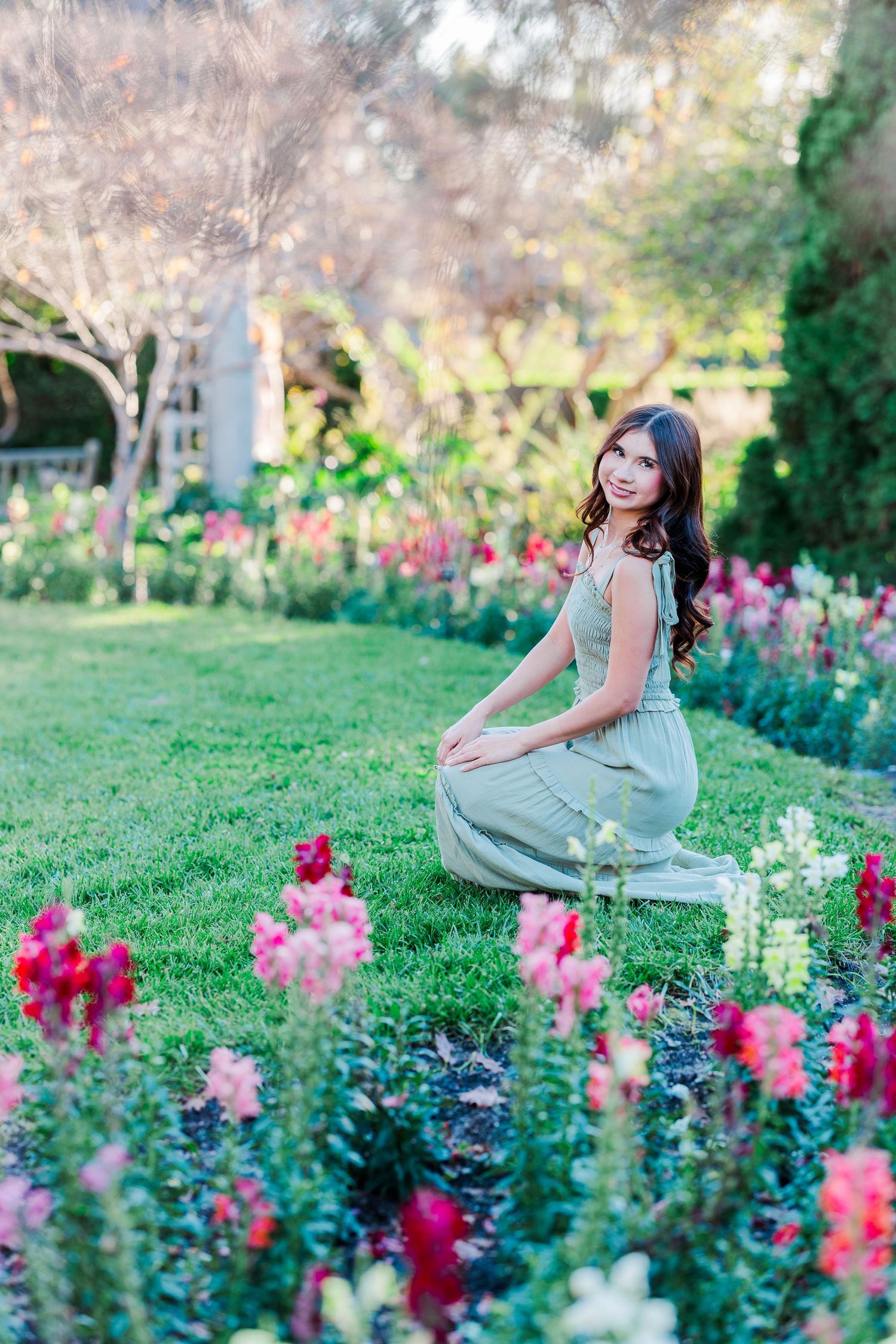 A woman in a mint green dress poses gracefully among vibrant pink snapdragon flowers in a garden setting.
