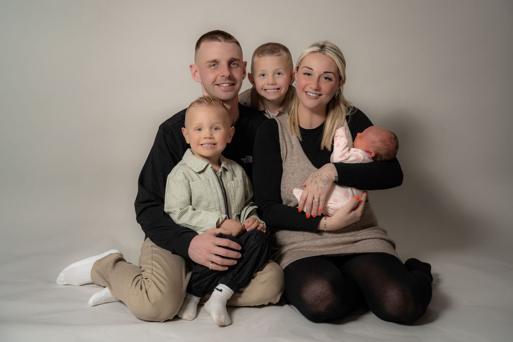 Family wearing neutral colored outfits poses together on floor in professional studio portrait session.