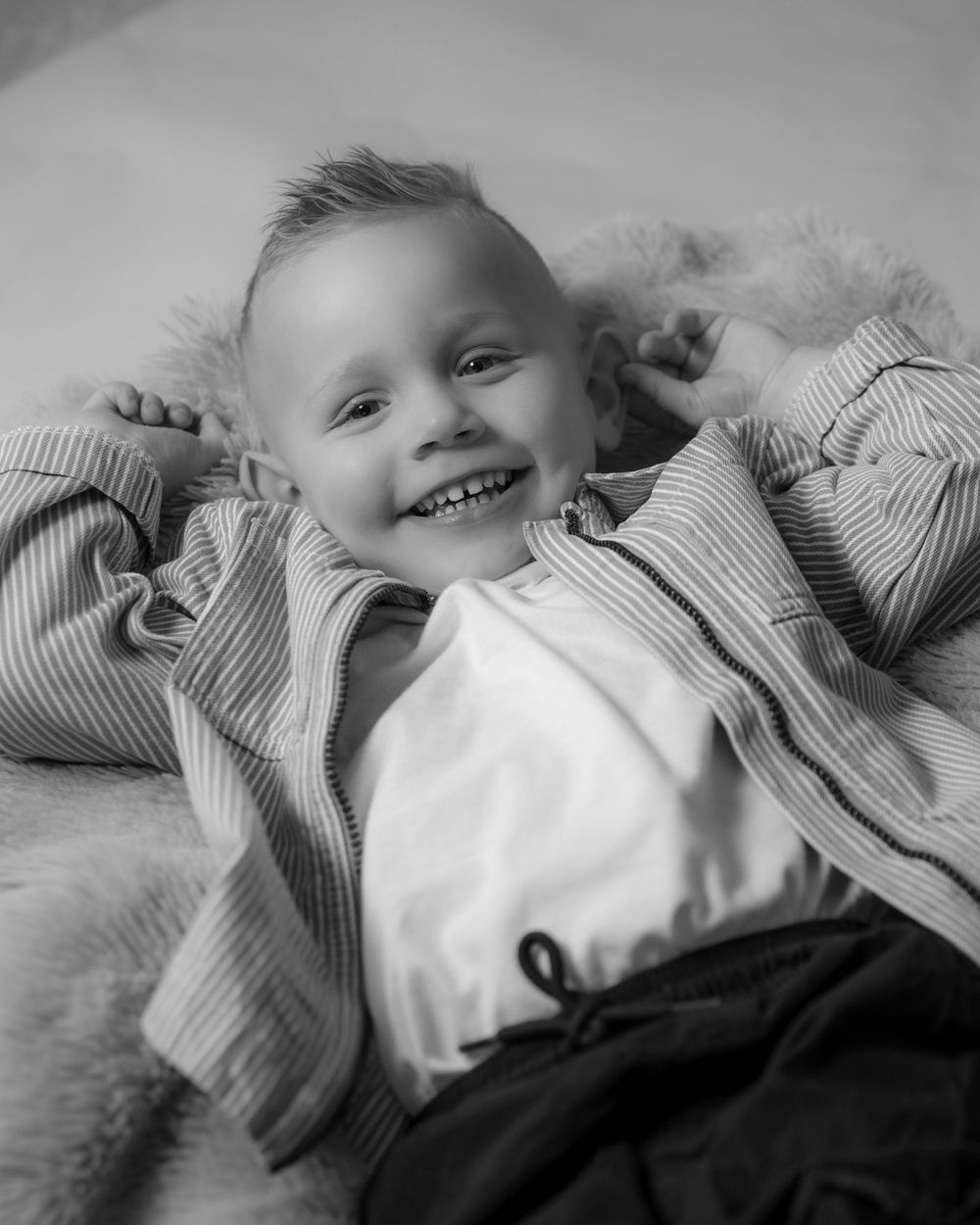 A black and white photo sequence showing a baby in a striped shirt lying down and smiling in different poses.