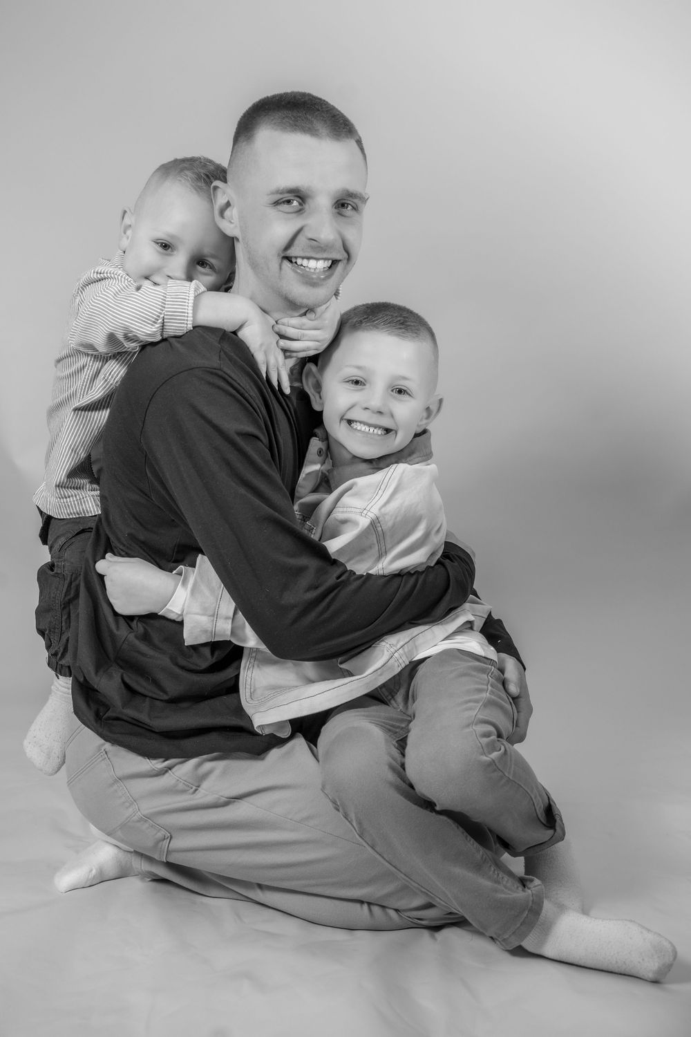 Black and white series of photos showing playful embrace between two people in casual clothing on light background.