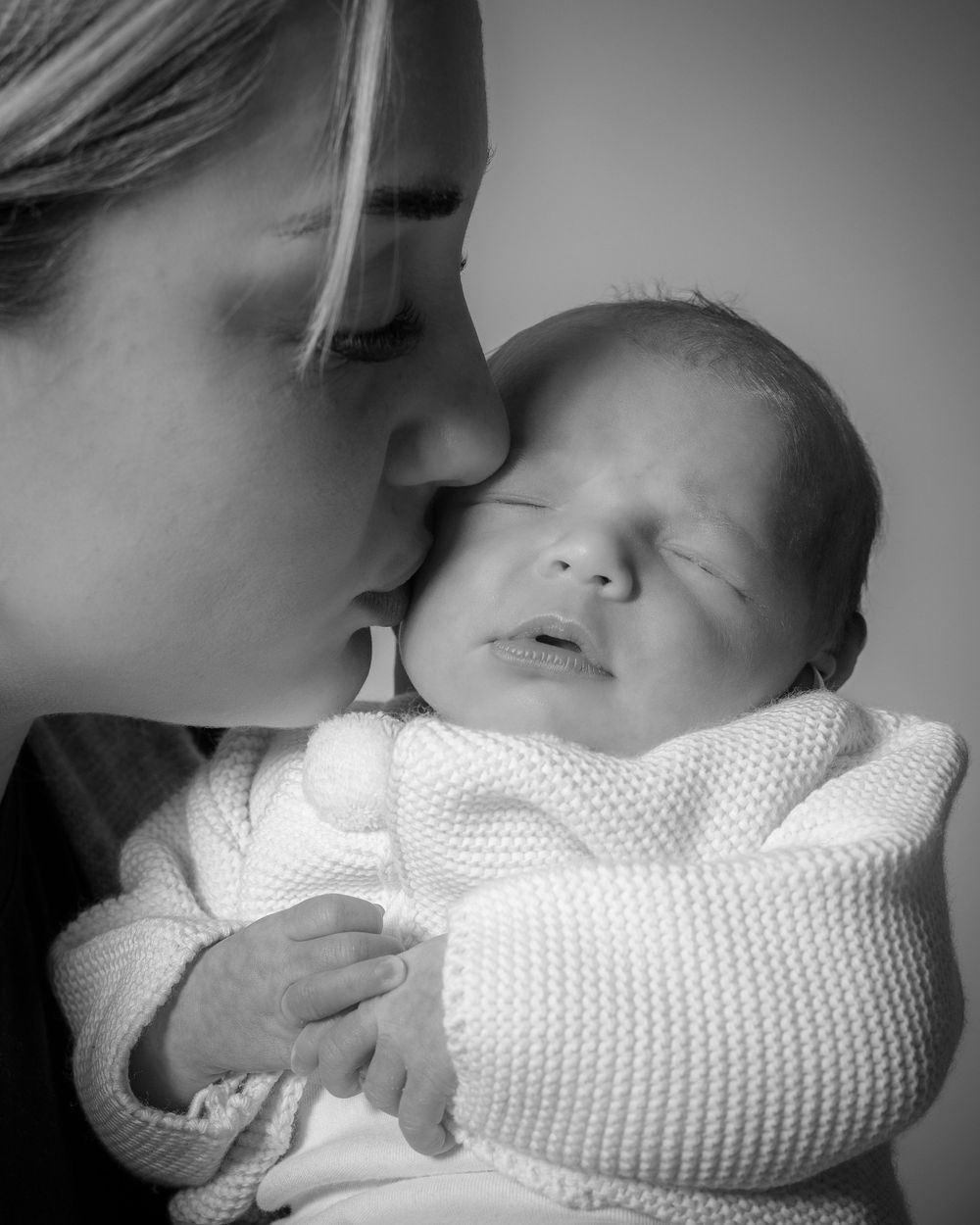 Black and white sequence of images showing a tender moment between a parent and sleeping infant in soft lighting.