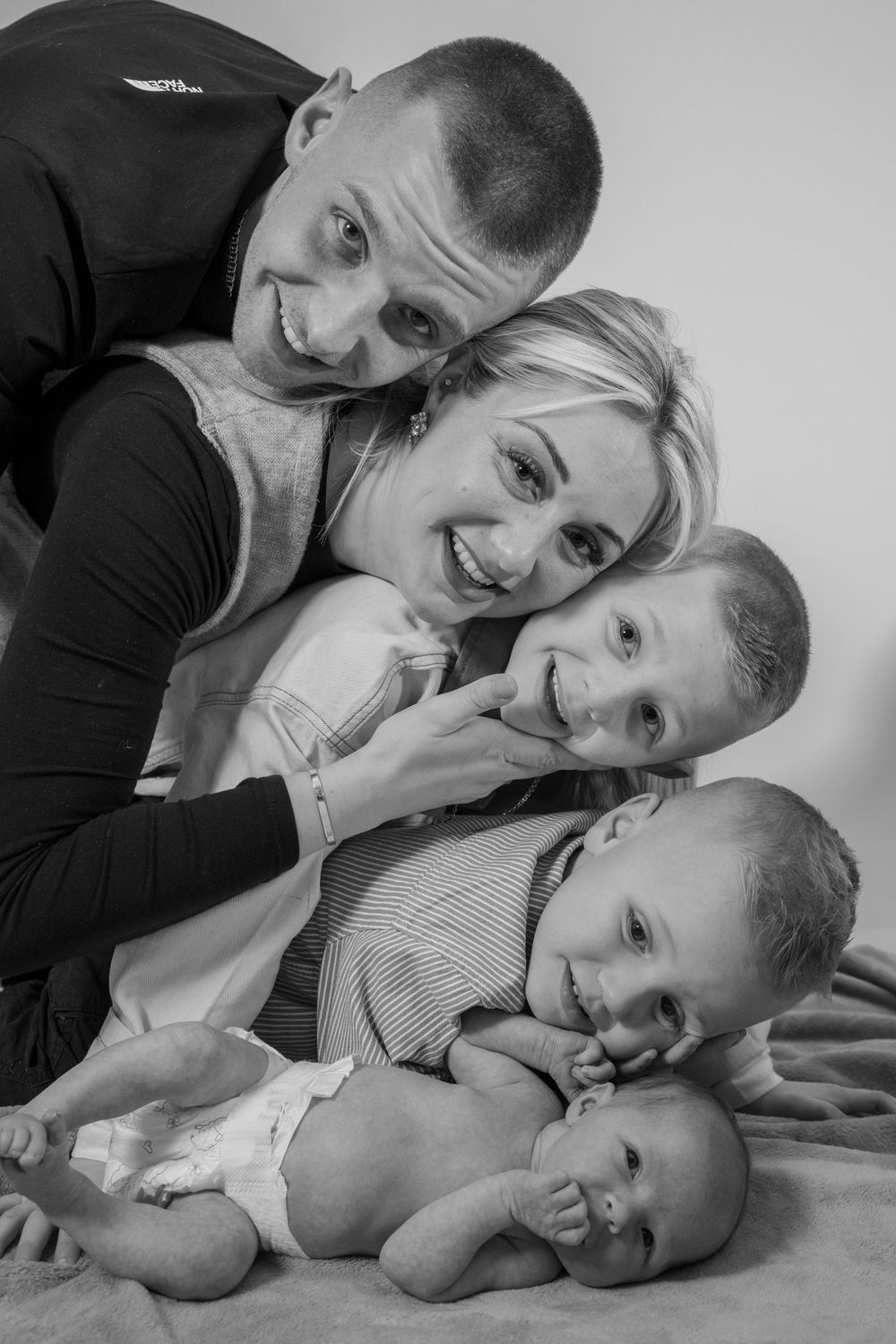Black and white portrait of a happy family with three children lying together and smiling at the camera.