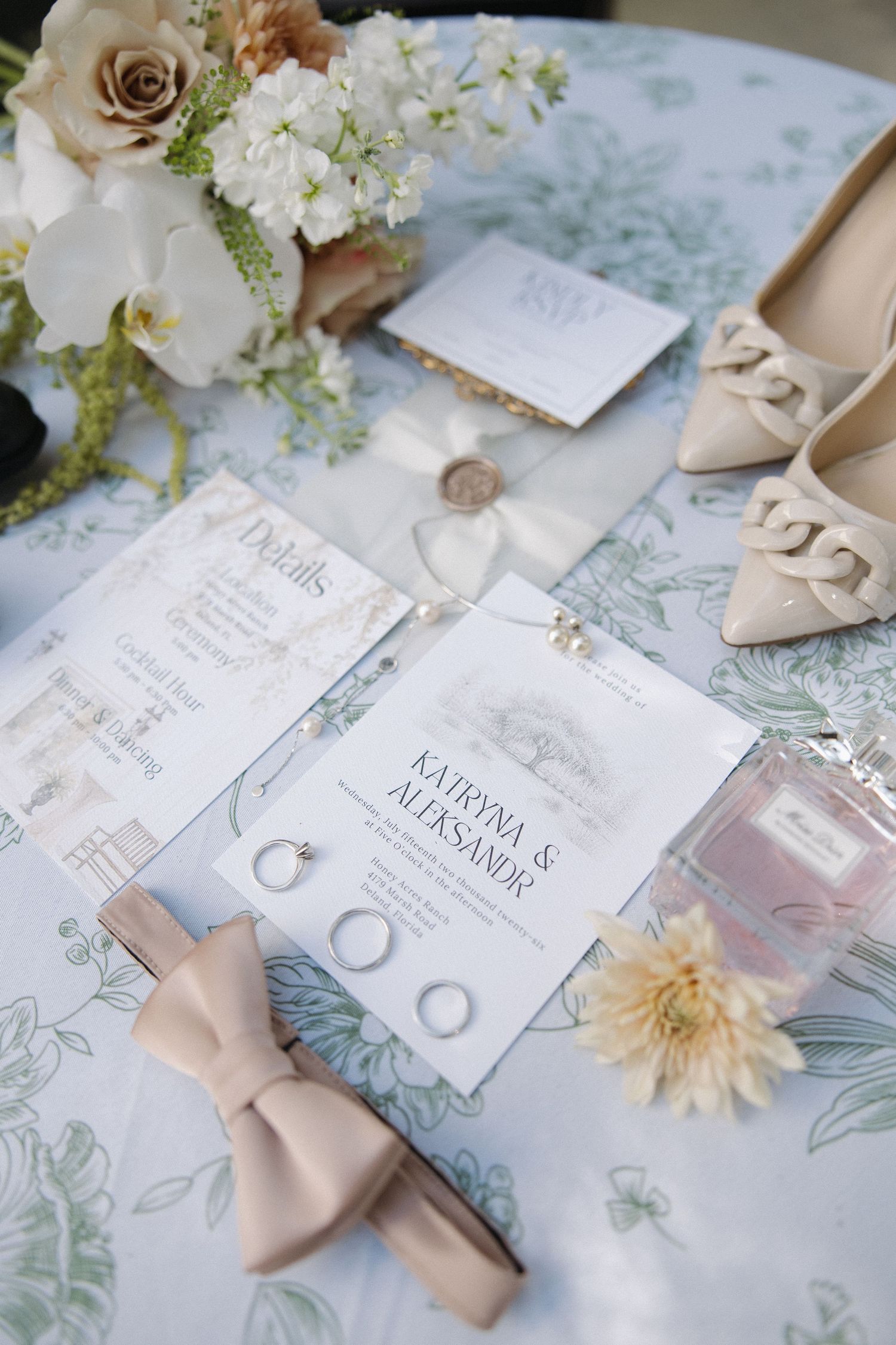 Flatlay of bridal accessories including white shoes, flowers, and orange accents on dark background.