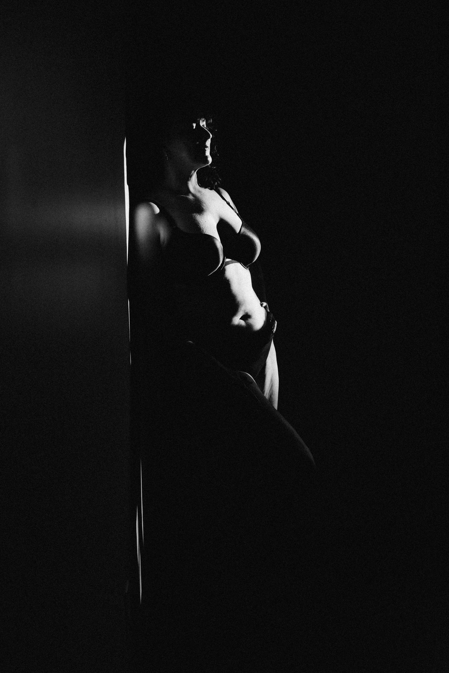 Black and white silhouette of a  woman leaning against a wall in dramatic low-key lighting.