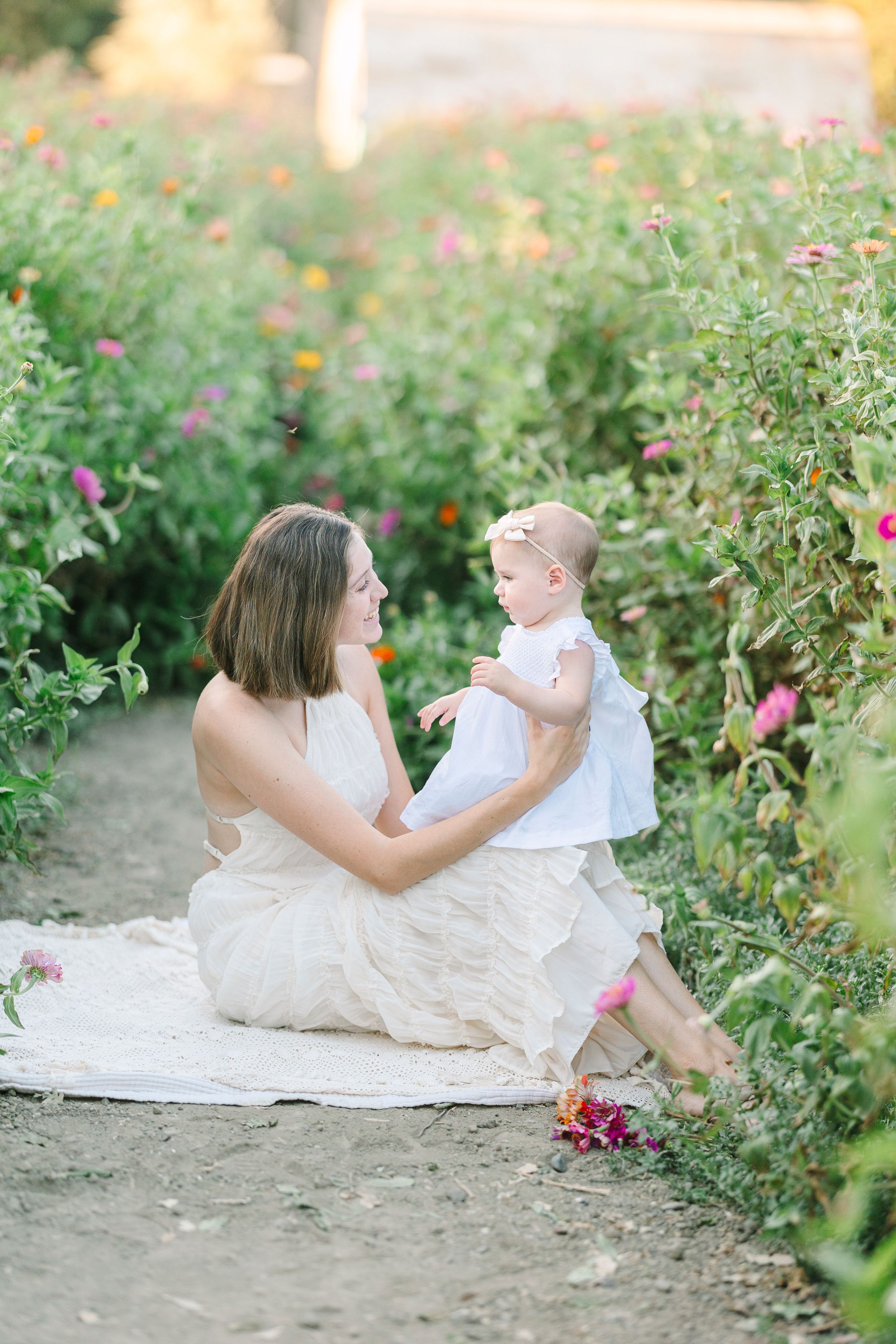 Mother and child share tender moments among blooming garden flowers at sunset.