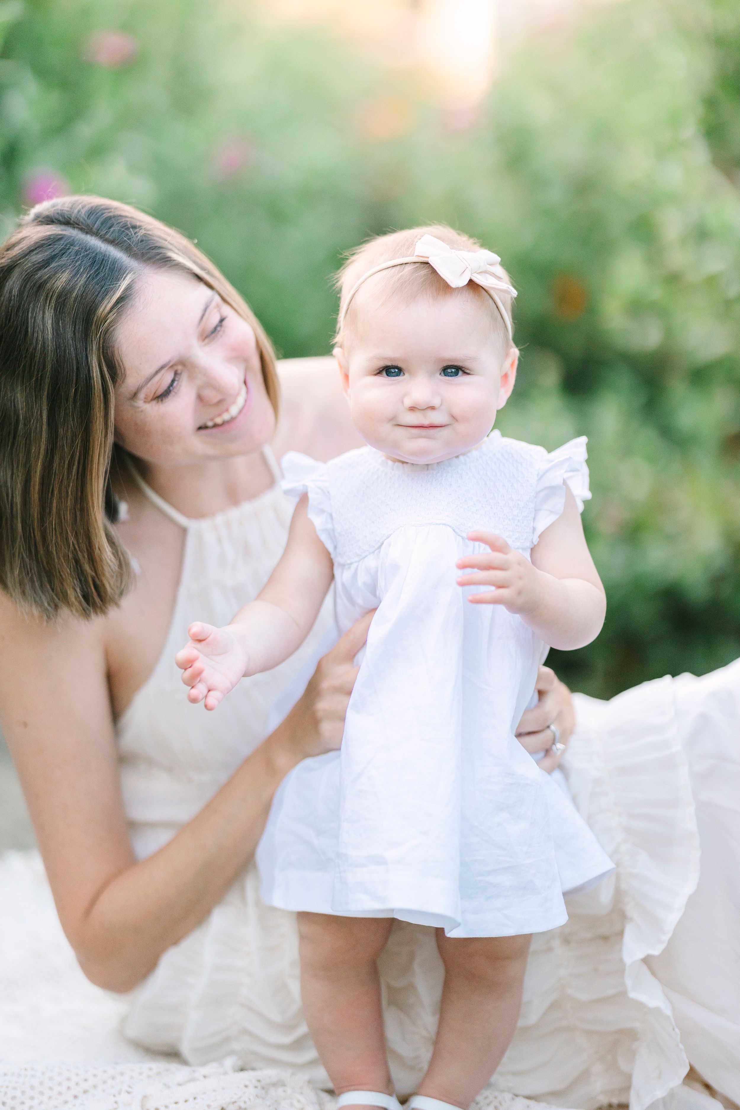A tender moment captured in white dresses against a soft garden backdrop.