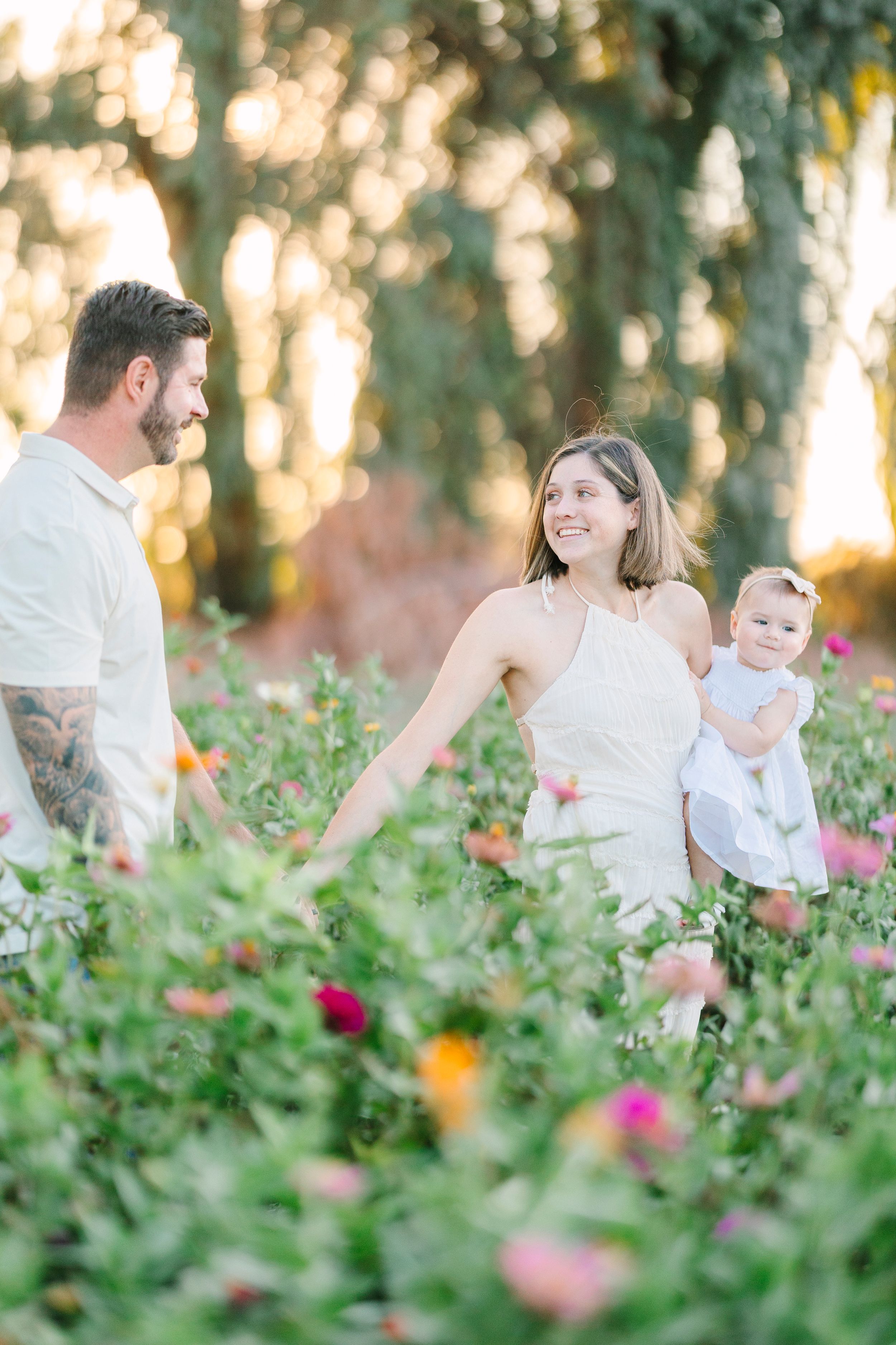 Family wearing white outfits poses together in a flowering garden at sunset.