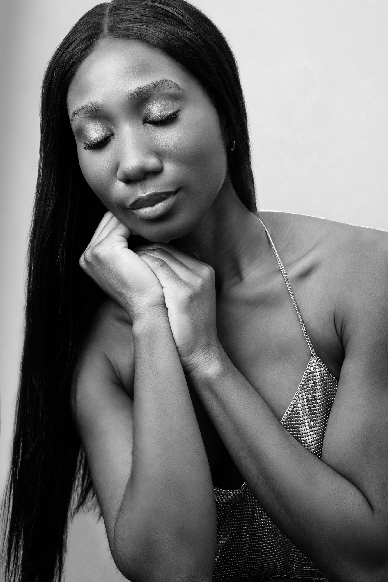 Black and white portrait of someone with long straight hair and closed eyes in contemplative pose wearing sparkly top.