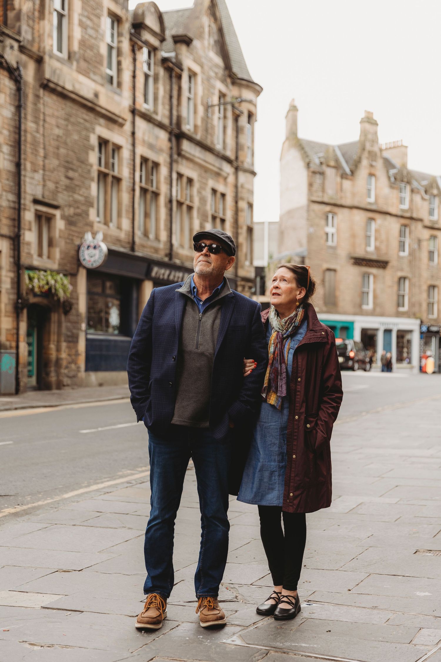 Three friends walking together on a historic stone street with old buildings in Edinburgh, Scotland.