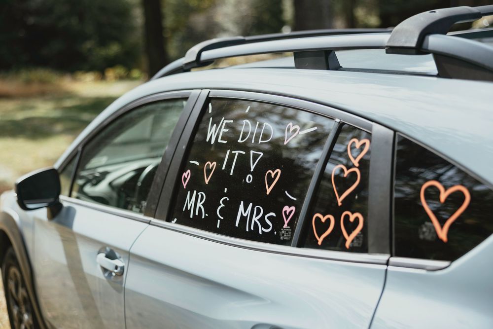 Car windows decorated with white text and heart drawings create a romantic wedding day display.