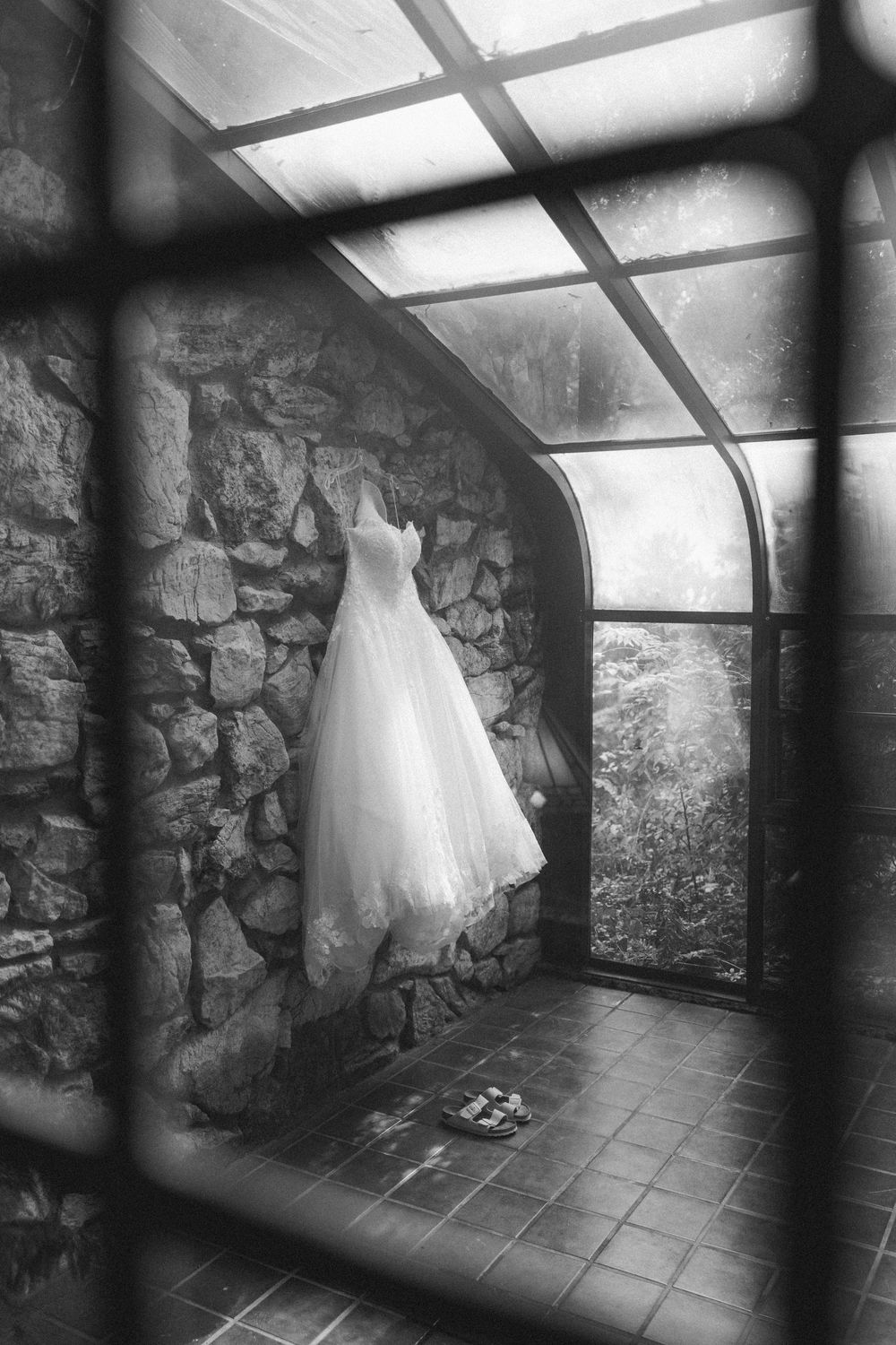 A white wedding dress hangs ethereally in a stone-walled room with dramatic lighting and skylights.
