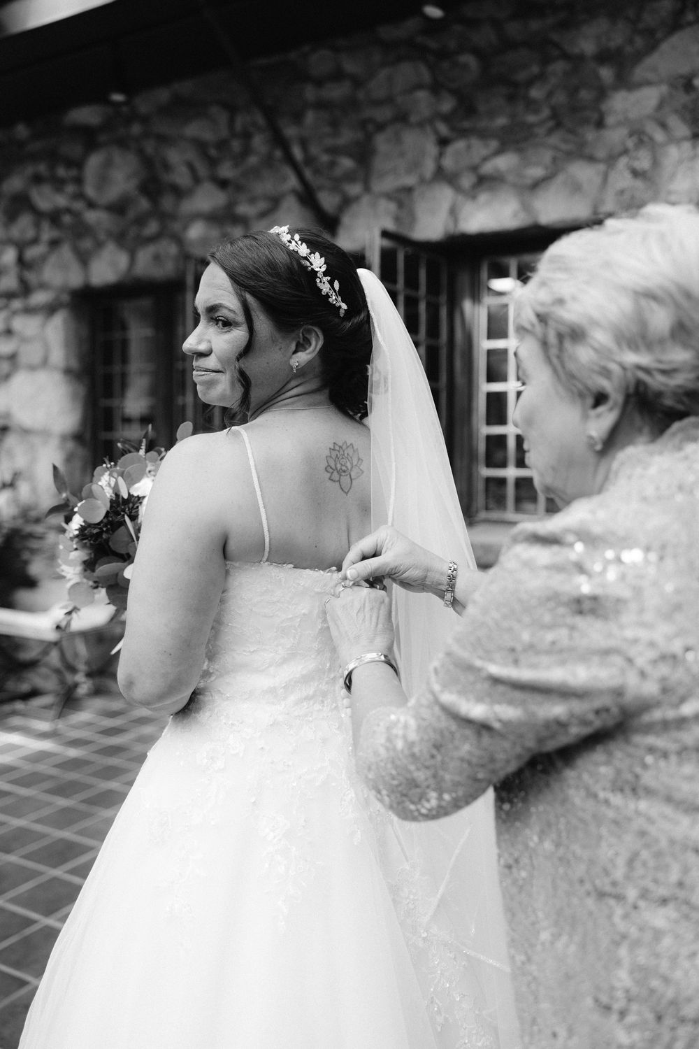 A delicate white wedding gown with lace details photographed against a rustic stone wall background.
