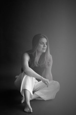 Black and white portrait of a person in white clothing seated on the floor in a contemplative pose.