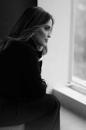 A dramatic black and white profile silhouette of a woman with long dark hair gazing pensively out a bright window.
