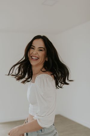 Candid portrait of a person in white top and jeans laughing with hair in motion.