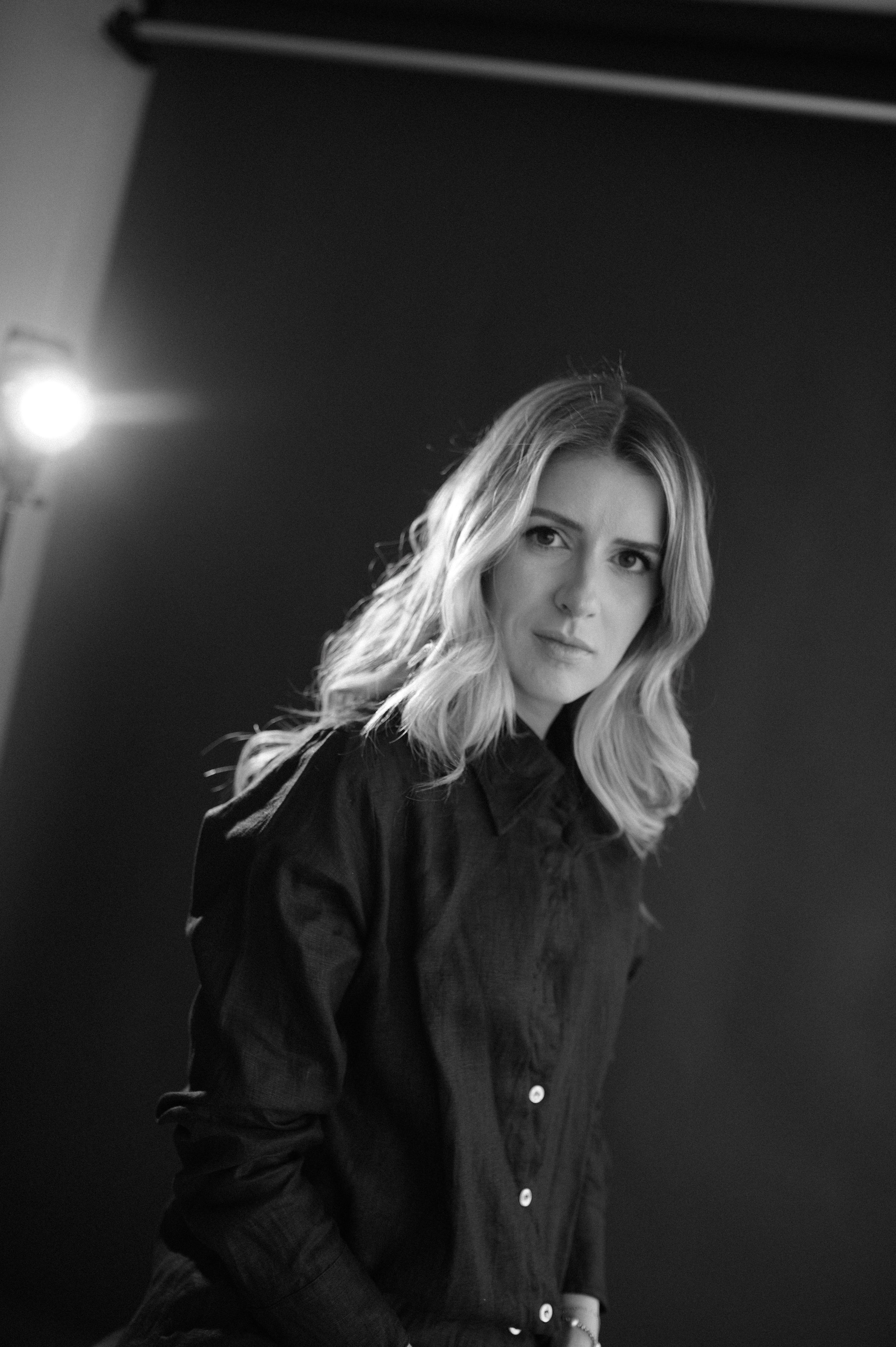 A dramatic black and white studio portrait with moody lighting features a subject in a dark button-down shirt.