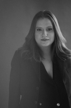 A black and white portrait photograph showing a person wearing a dark blazer against a simple background.