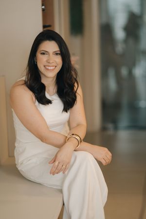 A person in a white sleeveless dress sits gracefully in a warm-lit indoor setting, creating an elegant portrait series.