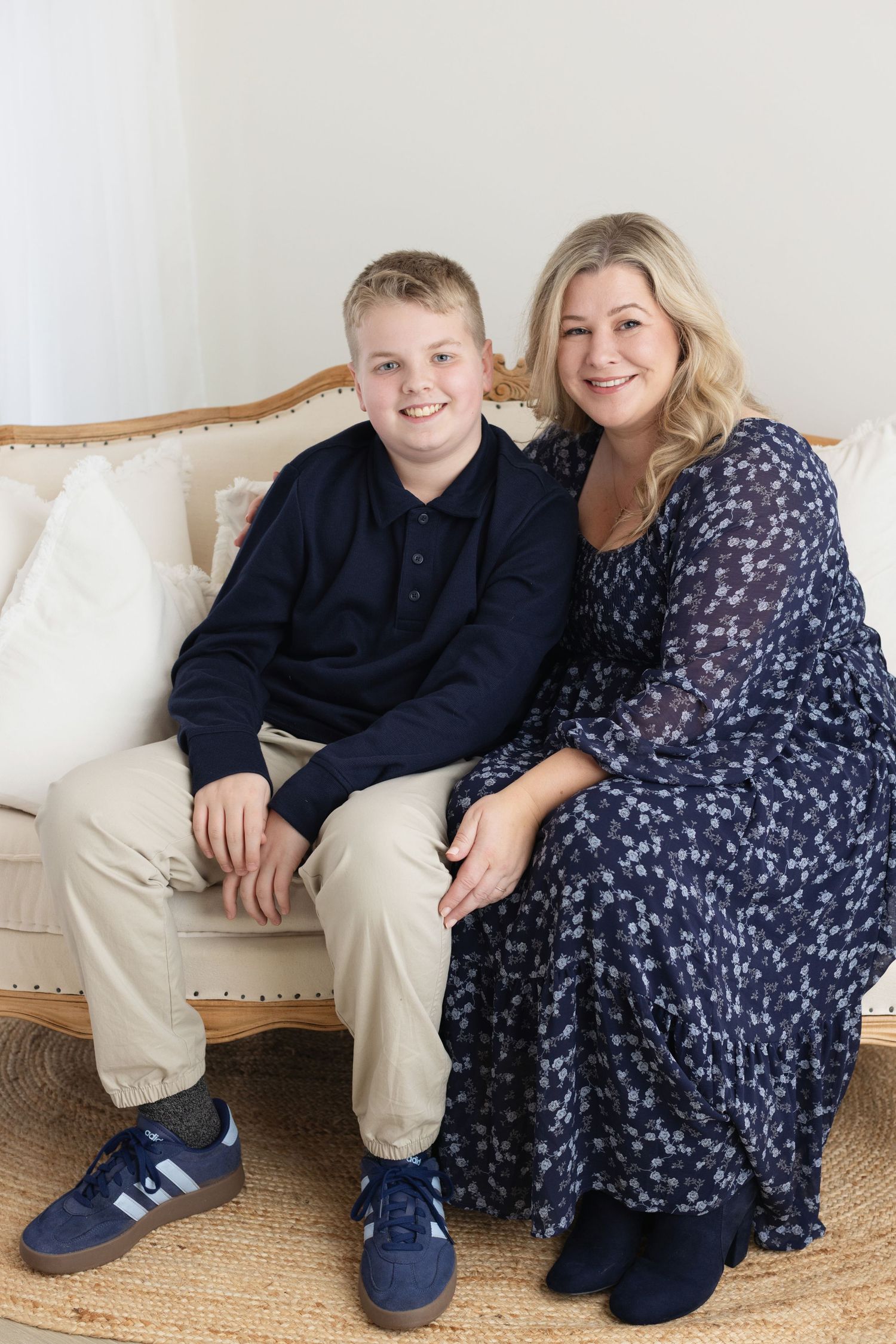 A pair sits together on a cream-colored sofa in coordinating navy outfits for a casual portrait session.