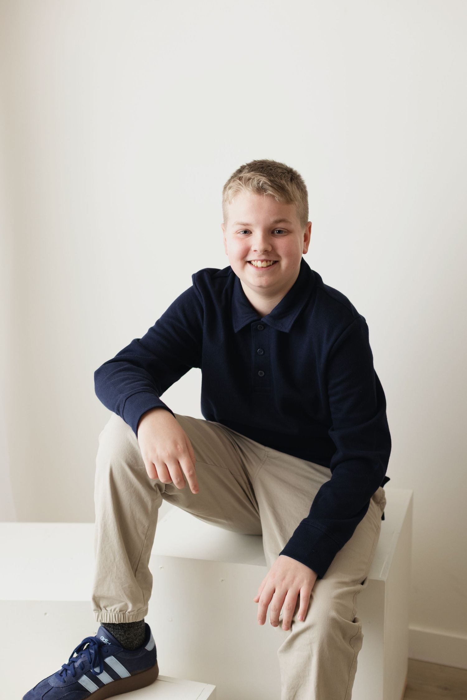 A person in a navy hoodie and khaki pants sits casually on white steps against a light background.